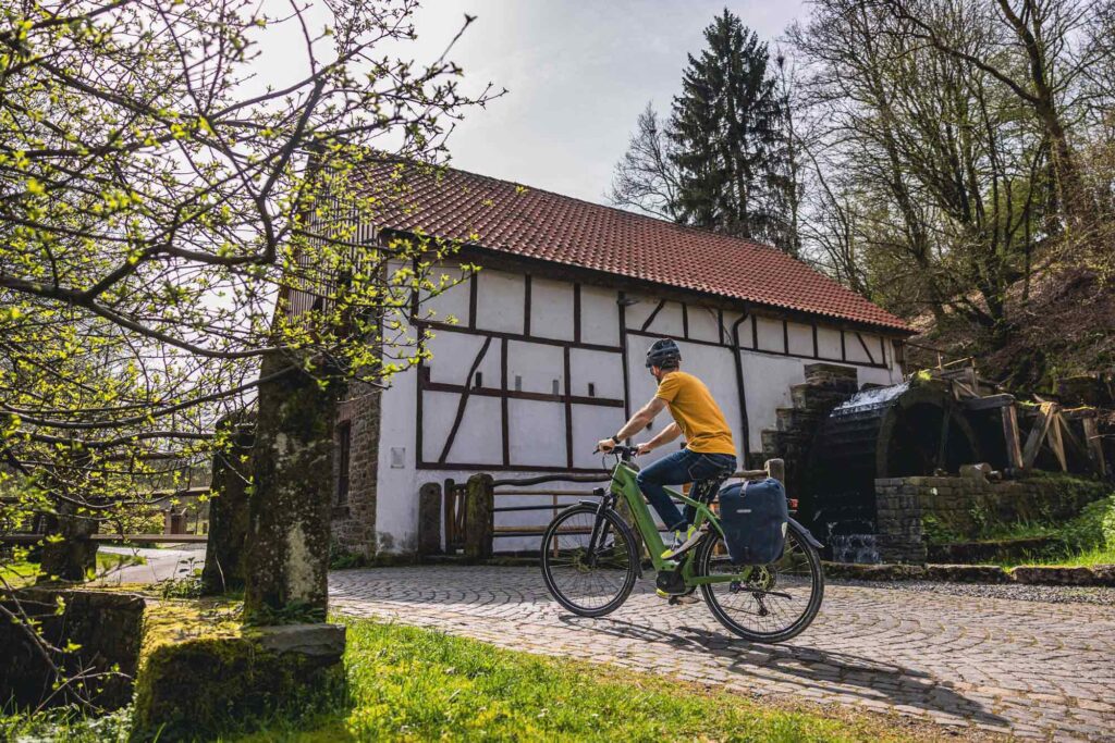 Radfahrer auf einem Pflasterweg bei einer Wassermühle